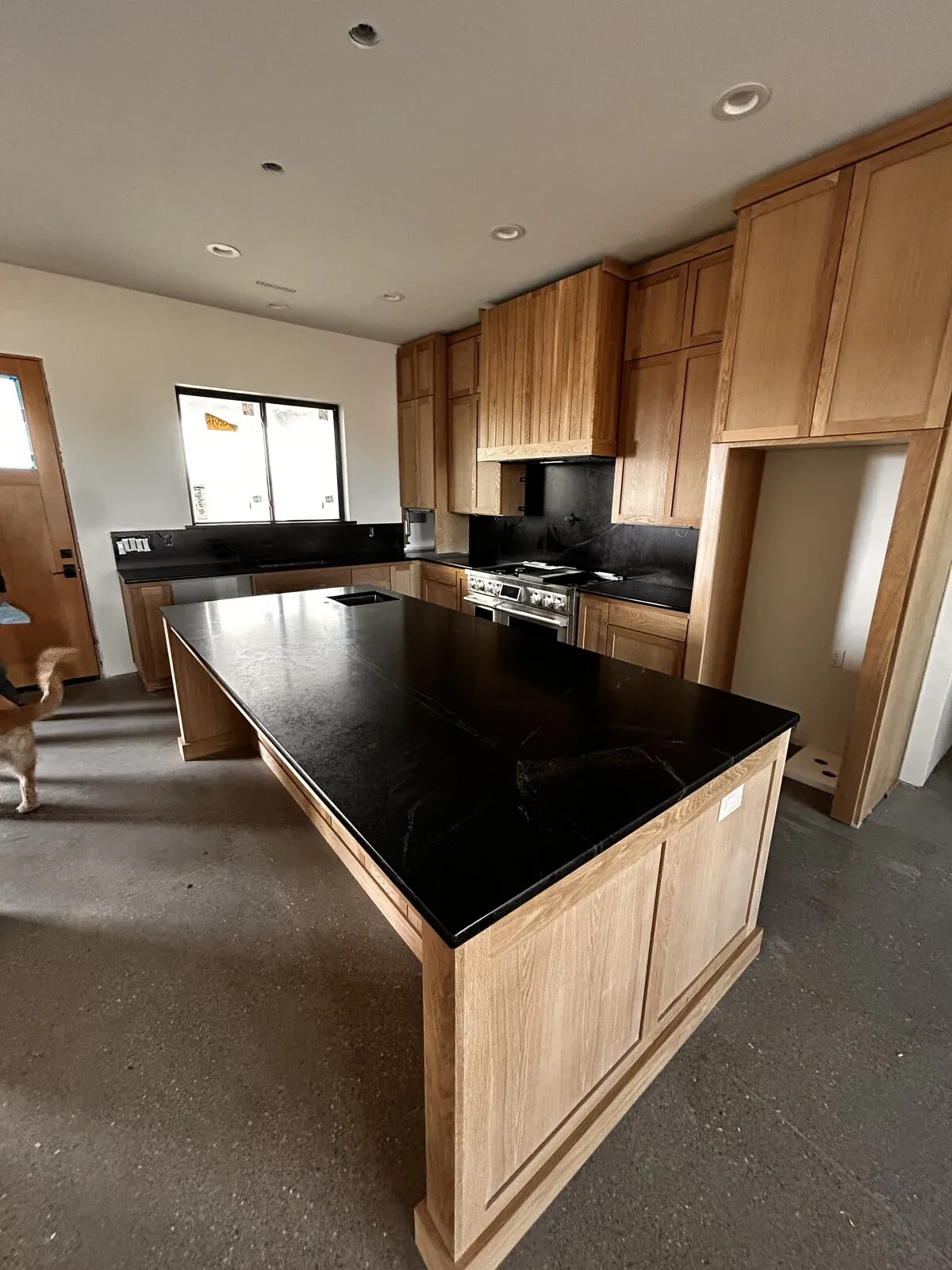Dark stone kitchen island with matching slab backsplash and white oak shaker cabinetry
