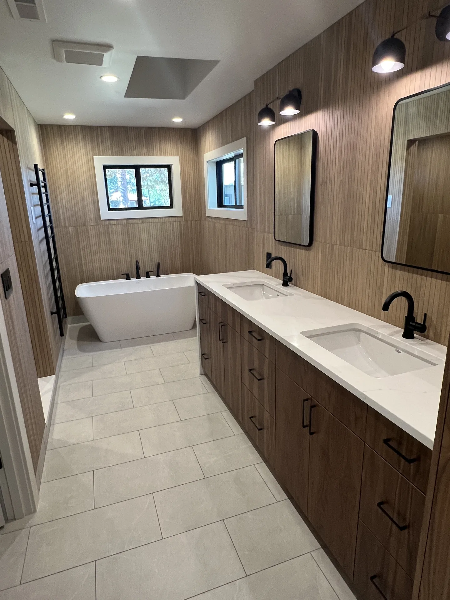 Master bathroom with freestanding soaking tub, wood-look tile walls and a long double vanity with white quartz countertop