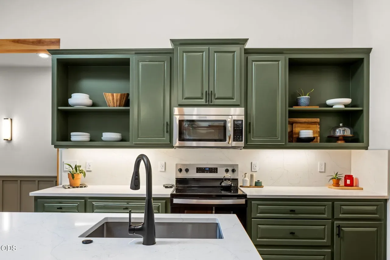 Kitchen with deep green shaker cabinets, open upper shelving, white quartz countertop with undermount sink and matte black faucet, and stainless range with microwave above