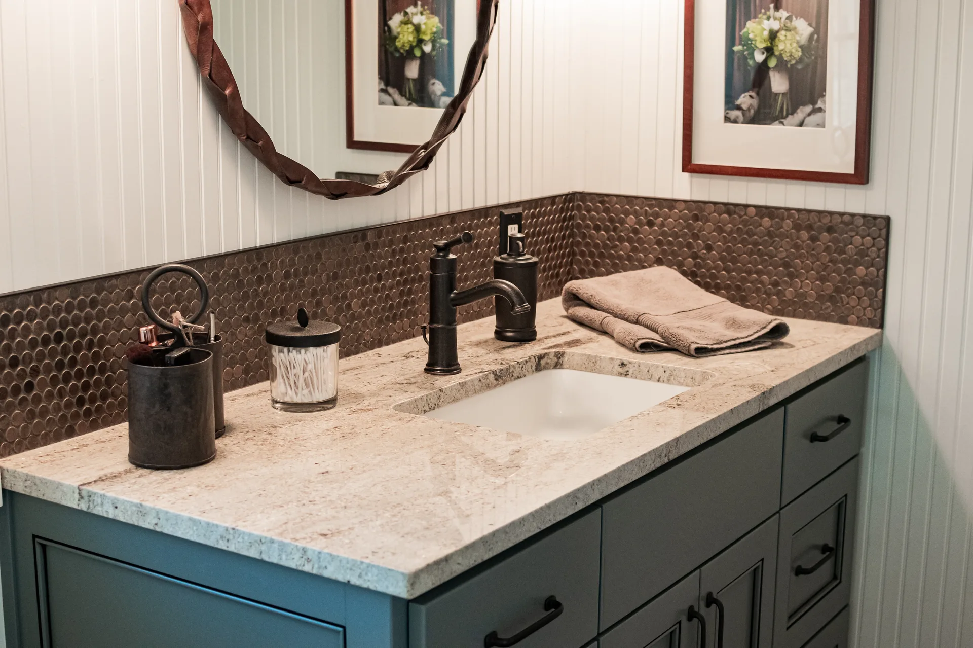 Light granite vanity with blue cabinets and copper mosaic backsplash