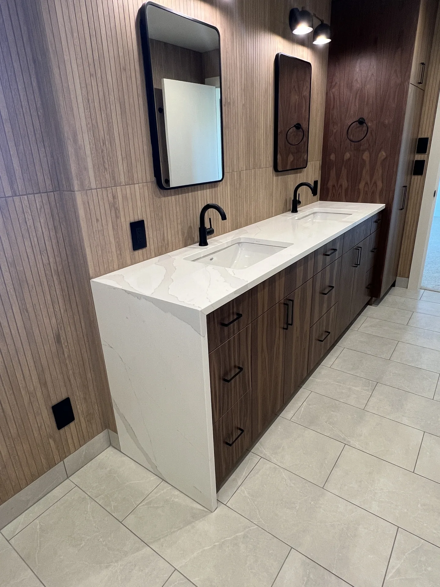 Long double vanity with white quartz countertop and waterfall end panel, dark wood cabinets and black-framed mirrors