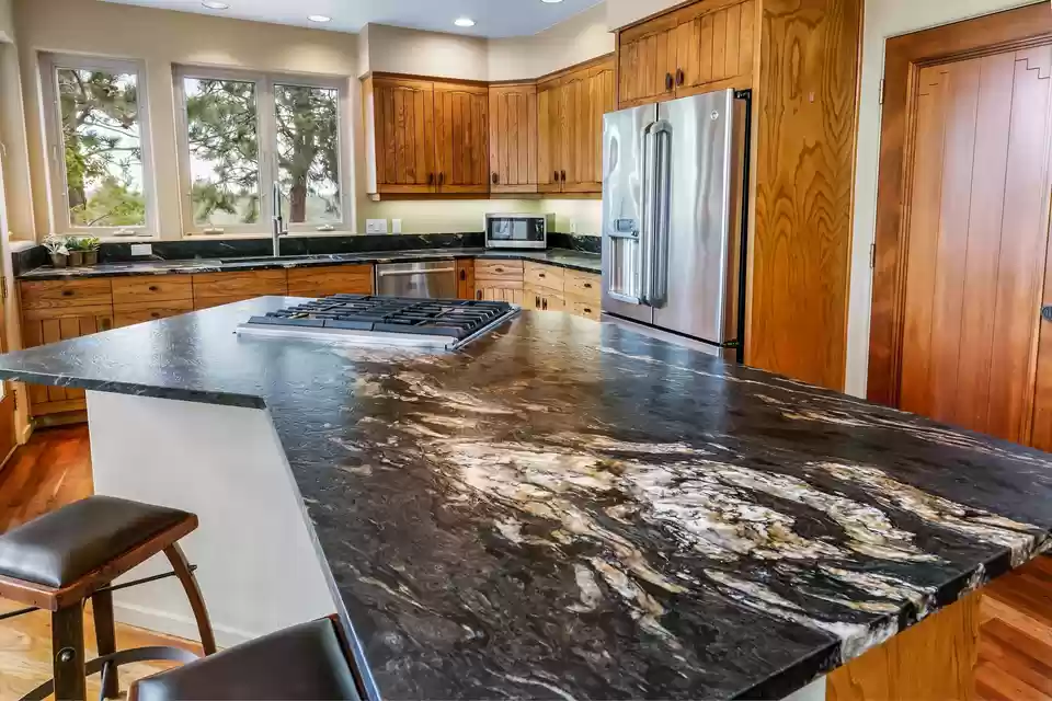 Dark stone kitchen island with gold and cream veining, integrated cooktop and knotty pine cabinetry