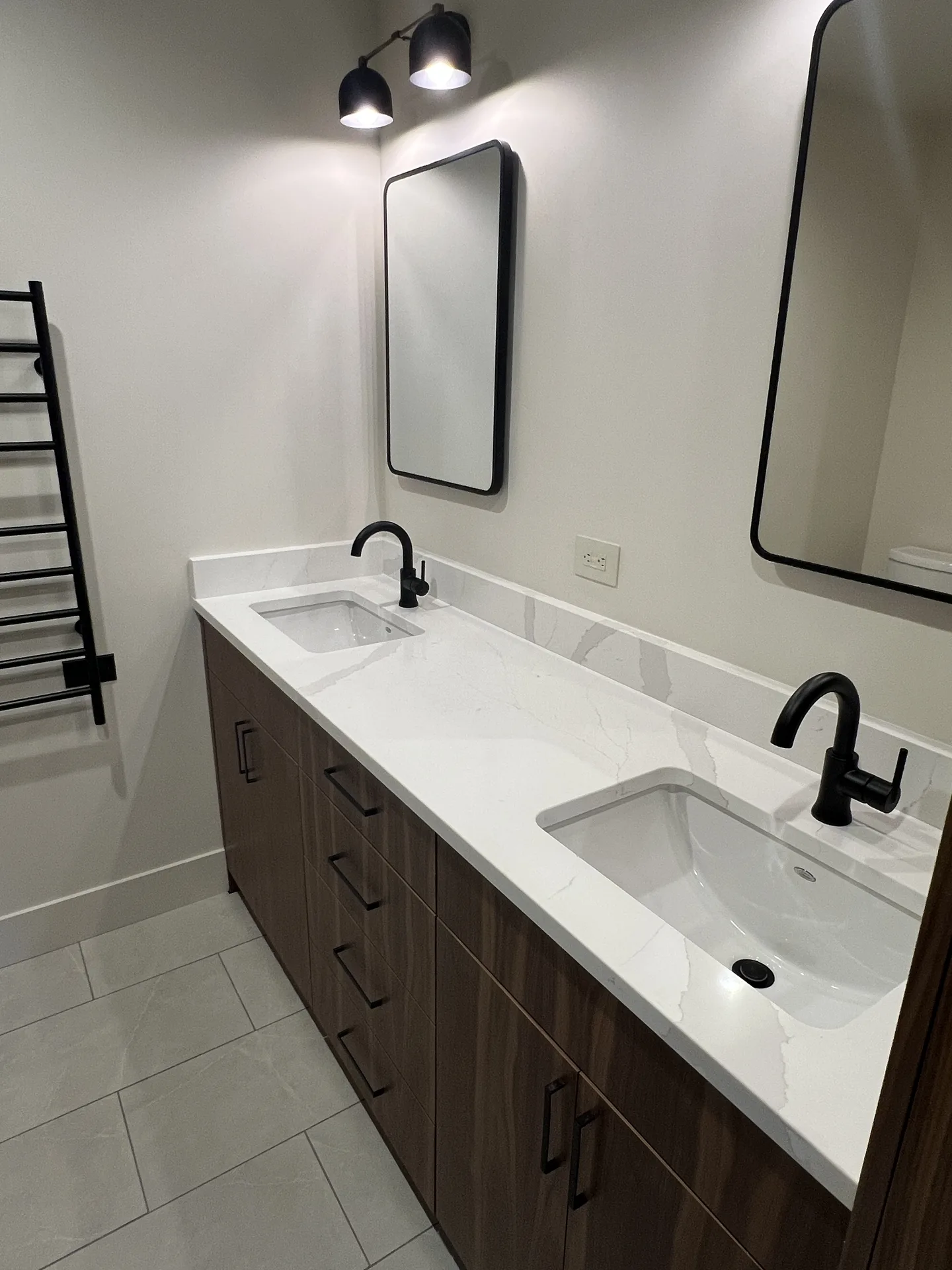 Bathroom double vanity with white quartz countertop and backsplash, dark wood cabinets, matte black faucets and two black-framed mirrors