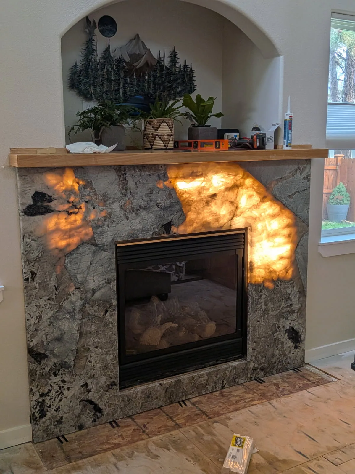 Backlit translucent stone fireplace surround and hearth with a wood mantel beneath an arched niche